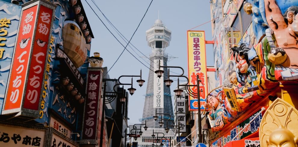 Lively street view in Osaka with vibrant shops and the iconic Tsutenkaku Tower in the background.