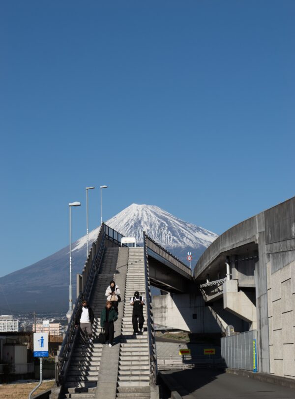 People walking on a staircase with Mount Fuji in the background under a clear sky.