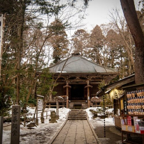 A tranquil scene of a traditional Japanese temple surrounded by trees and snow.