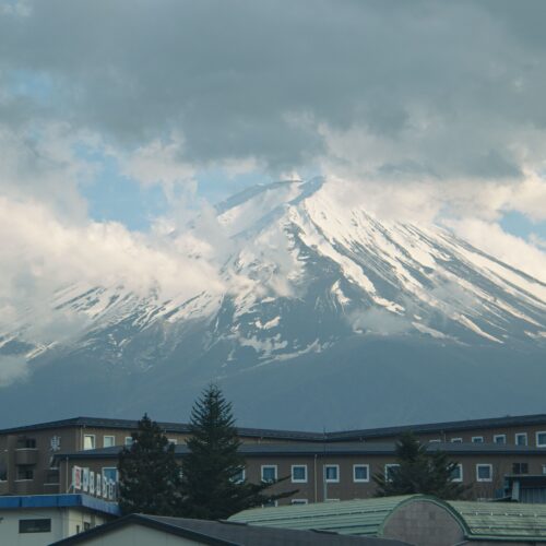 Breathtaking view of Mount Fuji partially covered by clouds above a building.
