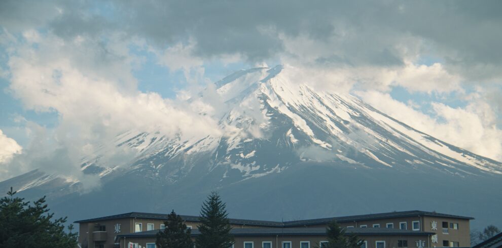 Breathtaking view of Mount Fuji partially covered by clouds above a building.