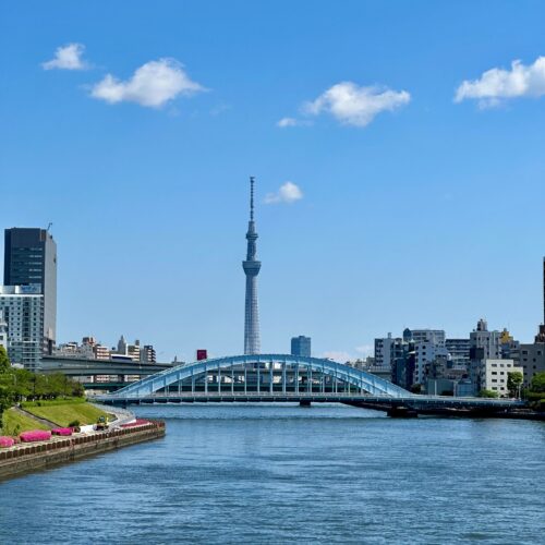 View of Tokyo Skytree and blue bridge over Sumida River in a bright, clear day.