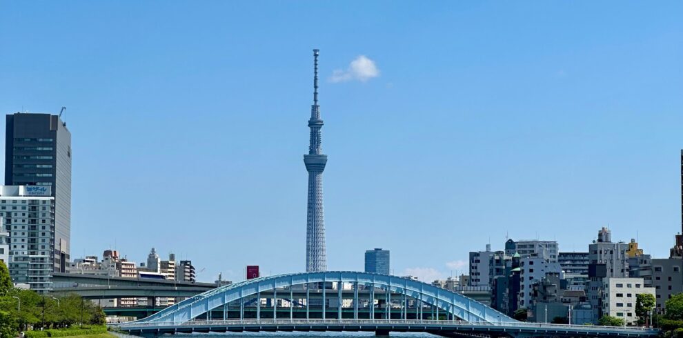 View of Tokyo Skytree and blue bridge over Sumida River in a bright, clear day.
