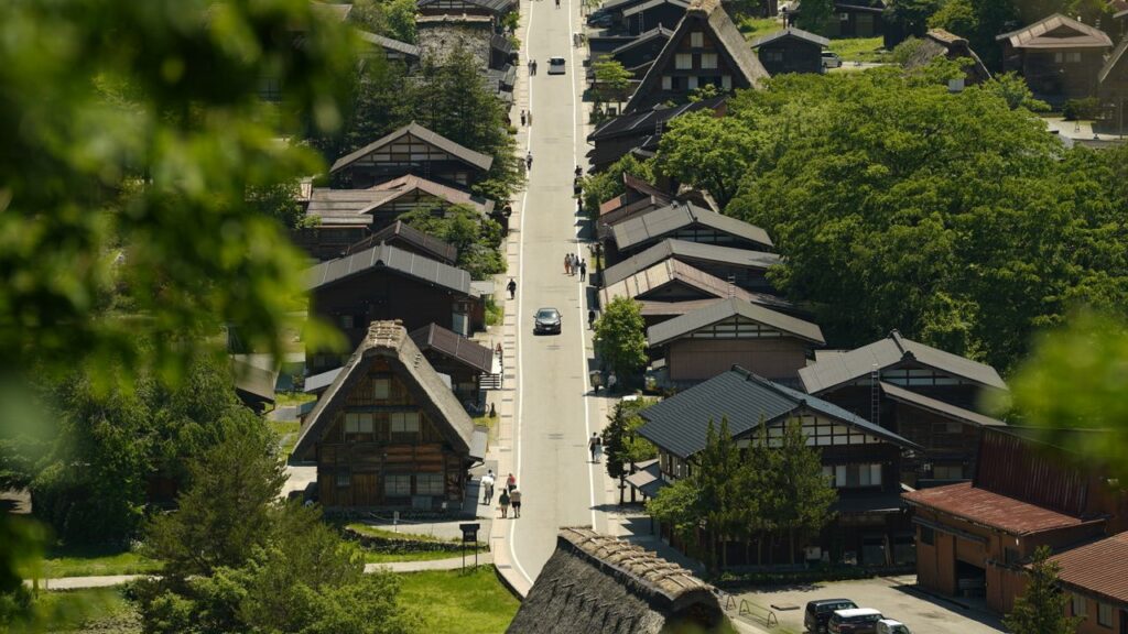 Trip Search Result Aerial view of Shirakawa village featuring traditional Gassho-Zukuri farmhouses surrounded by lush greenery.