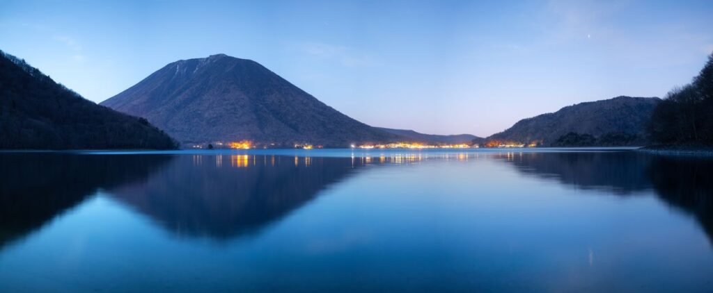 Trip Search Result Beautiful night view of Lake Chuzenji with Mount Nantai in Nikko, Japan reflecting lights over water.