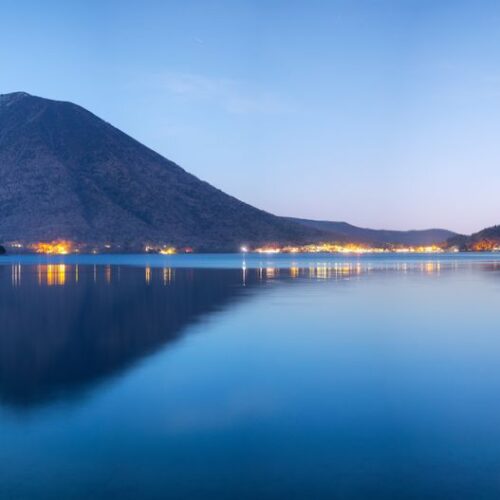 Beautiful night view of Lake Chuzenji with Mount Nantai in Nikko, Japan reflecting lights over water.