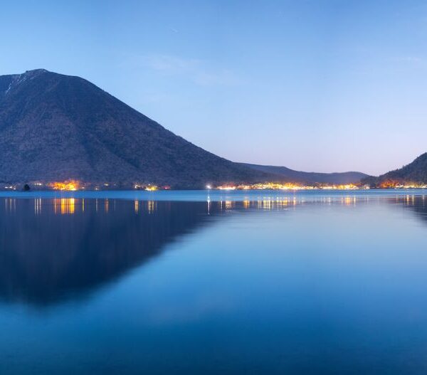 Beautiful night view of Lake Chuzenji with Mount Nantai in Nikko, Japan reflecting lights over water.