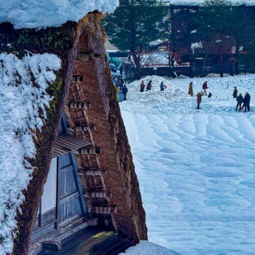 Snow-covered traditional Japanese house with people enjoying winter outdoors