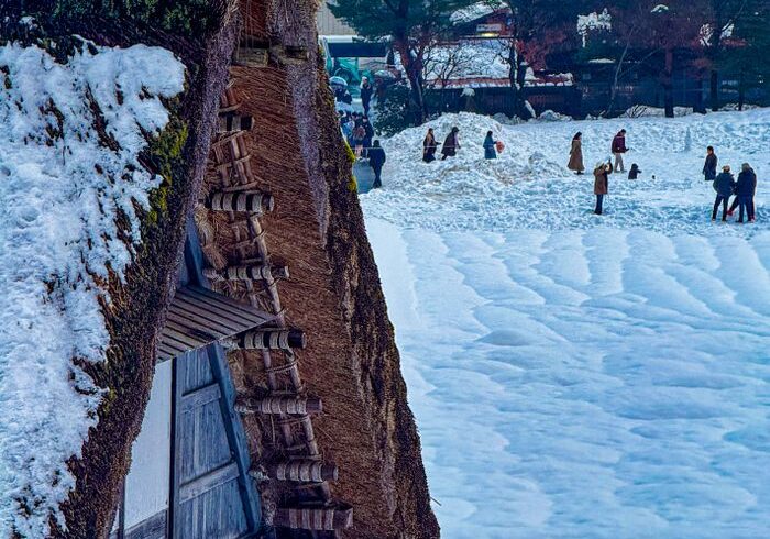 Snow-covered traditional Japanese house with people enjoying winter outdoors