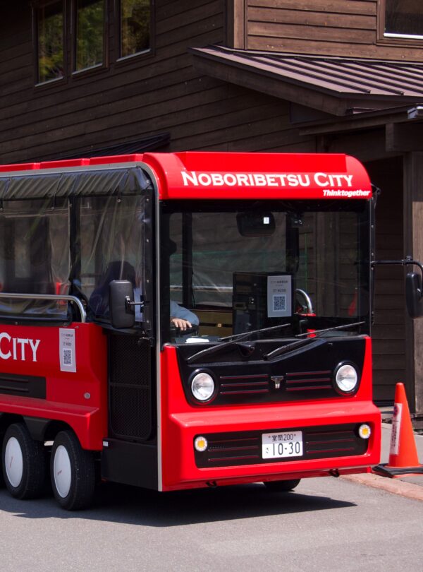 Tourist bus in Noboribetsu City, Japan, parked in front of a wooden building on a sunny day.