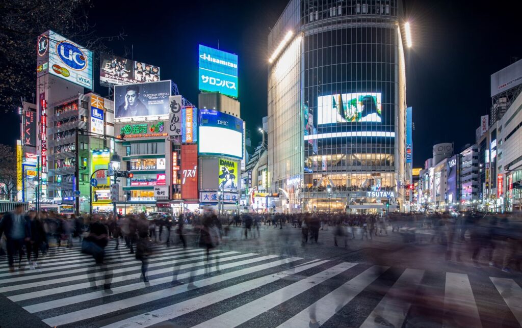 Trip Search Result Blurred pedestrians at night crossing in Shibuya, Tokyo, with vibrant city lights and bustling atmosphere.