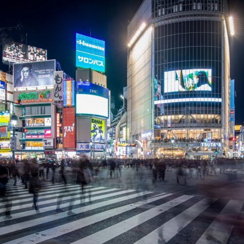 Blurred pedestrians at night crossing in Shibuya, Tokyo, with vibrant city lights and bustling atmosphere.