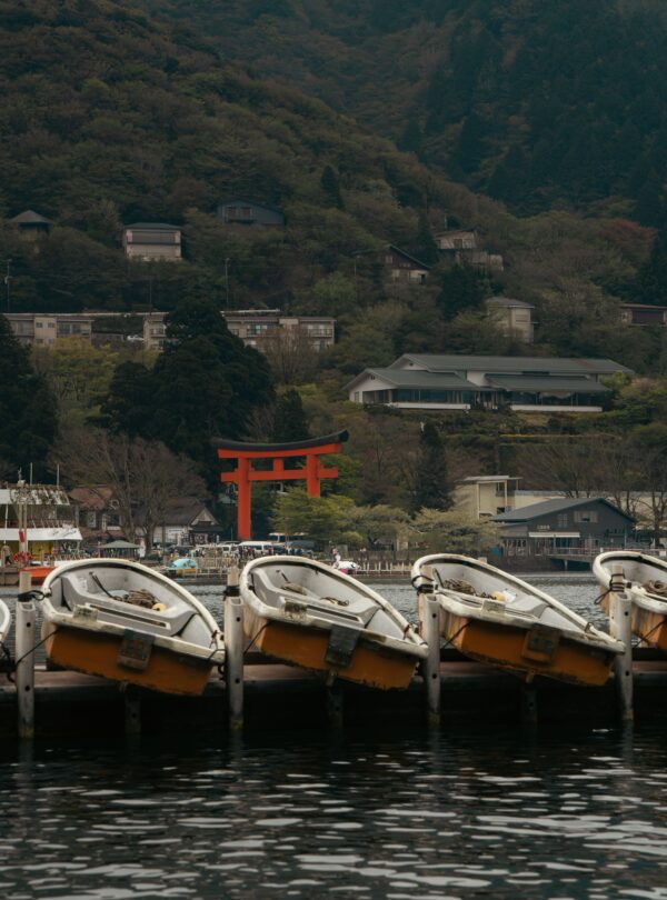 Scenic view of rowboats on Lake Ashi, Hakone, with iconic red torii gate amidst lush greenery.
