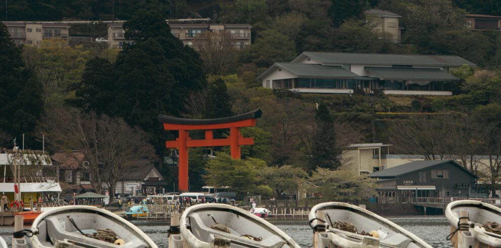 Scenic view of rowboats on Lake Ashi, Hakone, with iconic red torii gate amidst lush greenery.