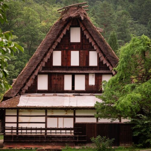 Scenic view of historic Gassho-Zukuri farmhouse surrounded by lush greenery in Takayama, Japan.