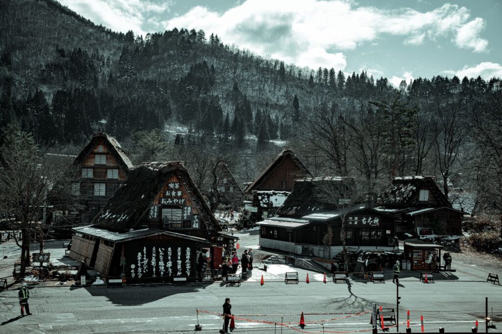 Trip Search Result From above of old wooden houses near asphalt road and mountains with growing trees and unrecognizable people walking in village under sky with clouds