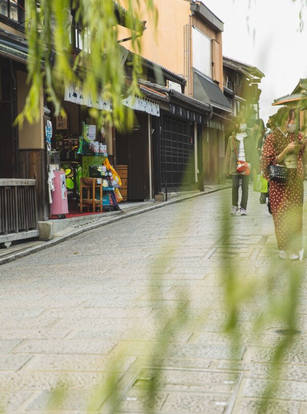Anonymous people in masks strolling on pavement street of city with oriental constructions