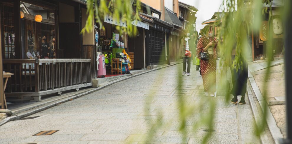 Anonymous people in masks strolling on pavement street of city with oriental constructions
